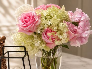 Pink and white flowers in a glass vase with a decorative bulb lamp.