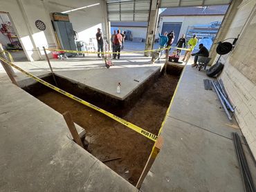 Construction site with a large rectangular trench and workers in a workshop.
