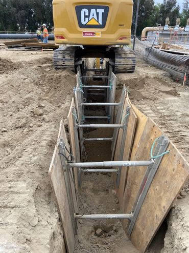 A CAT excavator working on a deep trench with safety shoring installed.