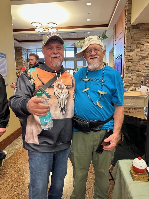 Two men smiling, one wearing a fish hat and fish necklace.