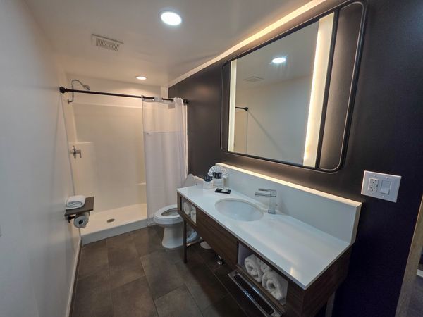 Modern bathroom with large mirror, white countertop, and shower area.