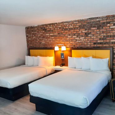 Two beds with yellow headboards against a brick wall in a modern hotel room.