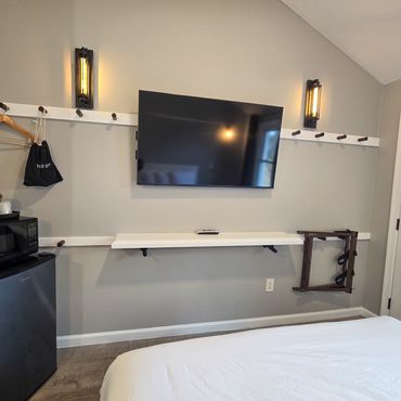Modern hotel room corner with TV, mini fridge, and wall hooks.