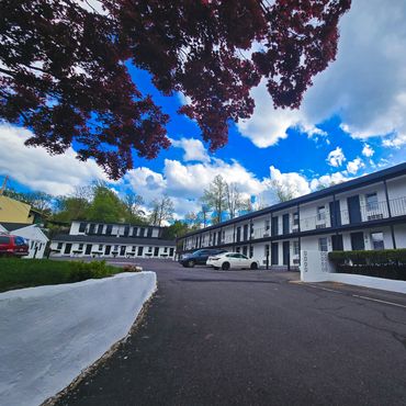 Motel complex under a vibrant blue sky with scattered clouds and leafy trees.