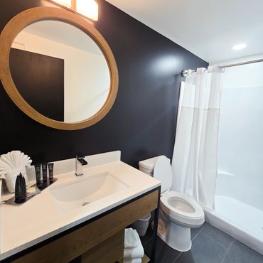 Modern bathroom with round mirror and black accent wall.