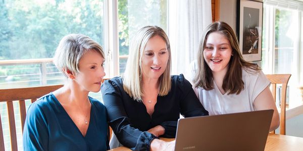 Three women looking at a laptop together, smiling and engaged.