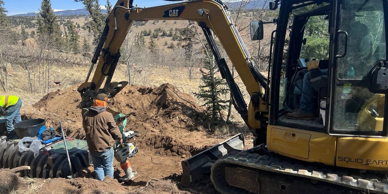 Workers using heavy machinery to dig and prepare the ground outdoors.