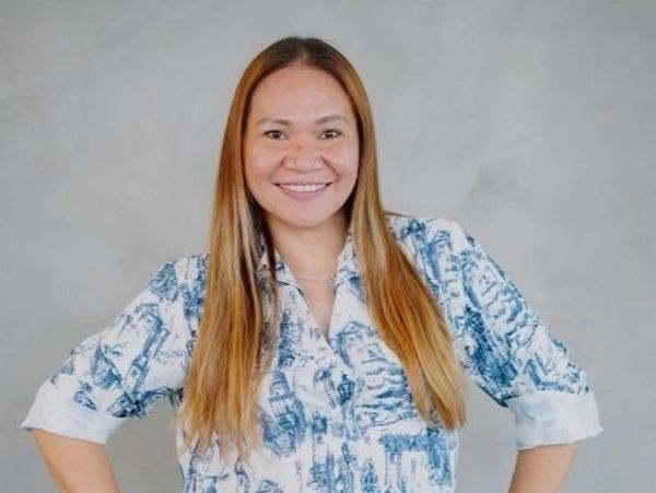Smiling woman in a patterned shirt with hands on hips.