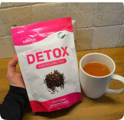 Hand holding a bag of Detox energizing tea with a cup of tea.