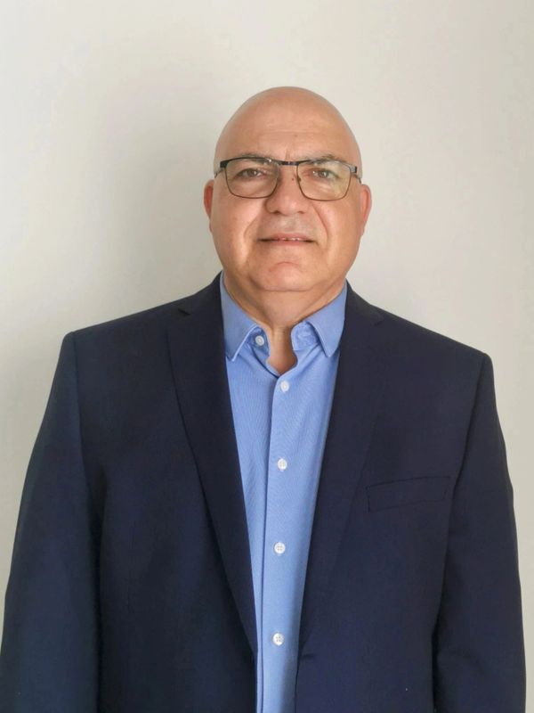 A bald man wearing glasses and a navy blue suit jacket with a light blue shirt.