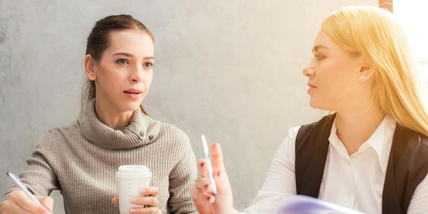 Two women having a conversation over coffee and notes.