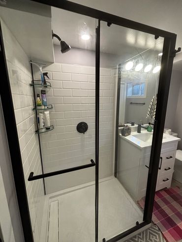 Modern bathroom shower with glass door and white tile walls.