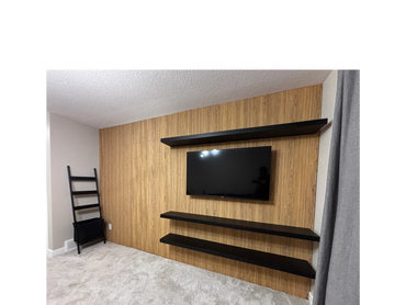 Modern living room wall with mounted TV and black shelves on wood paneling.