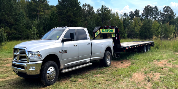Silver Ram 3500 truck with a Gator flatbed trailer on a grassy field.
