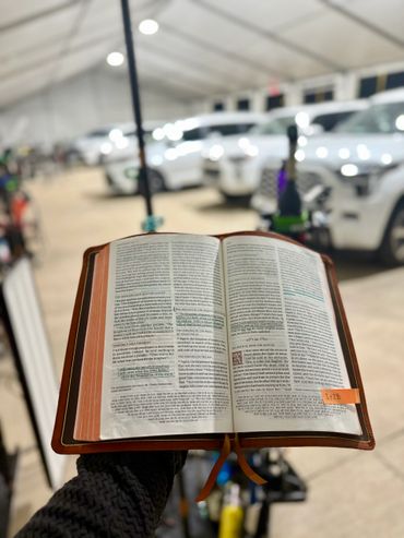 Open Bible held with highlighted text in a busy indoor setting with cars.