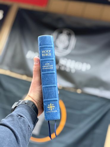 Hand holding a blue leather-bound Holy Bible with gold lettering.