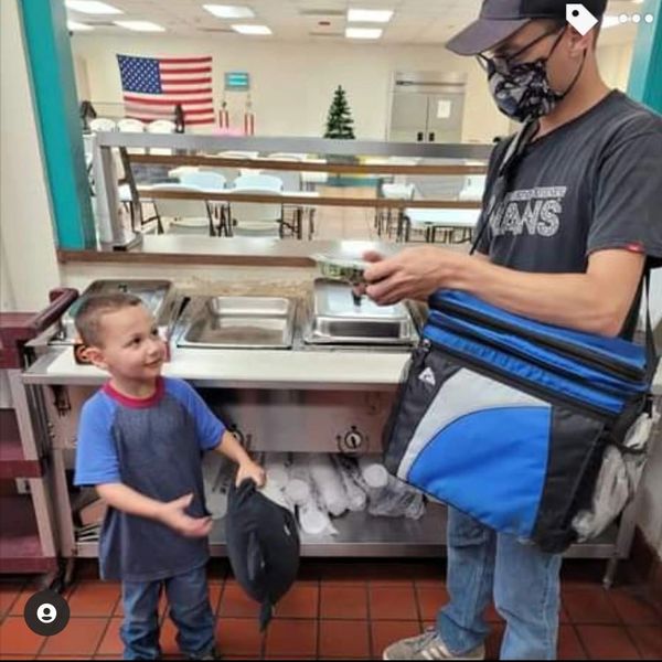 A young boy gives his cap to a masked food delivery person indoors.