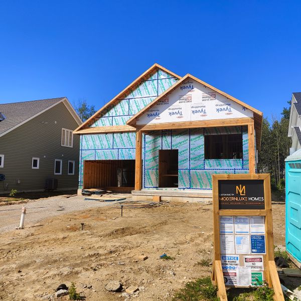 New house under construction with clear blue sky and nearby houses.