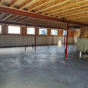 A basement under construction with freshly poured concrete floor and exposed beams.
