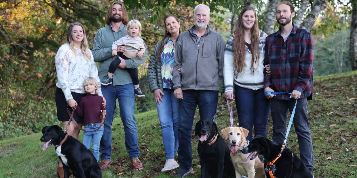 A large family with three dogs posing outdoors in autumn.