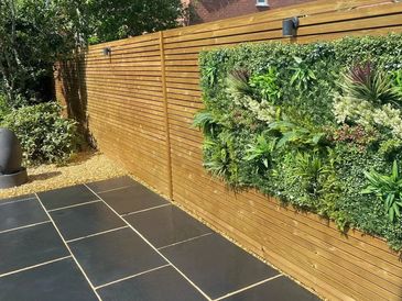 Horizontal timber slatted fence with green wall panel, black stone patio and gravel edging.