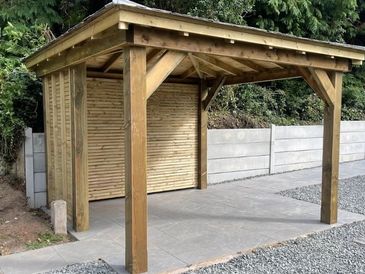 Outdoor timber pergola with slatted back panel on stone patio, set against leafy backdrop.