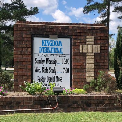 Church sign with worship and Bible study times and a stone cross.