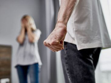 close-up photo of male fist, angry man and scared woman in the background