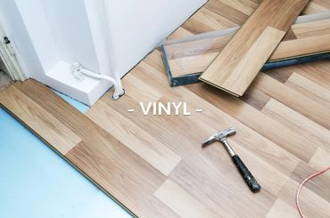 Vinyl flooring installation with hammer and planks near white wall.