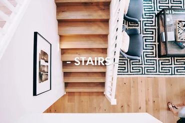 Top view of modern wooden stairs beside a patterned rug and blue chairs.