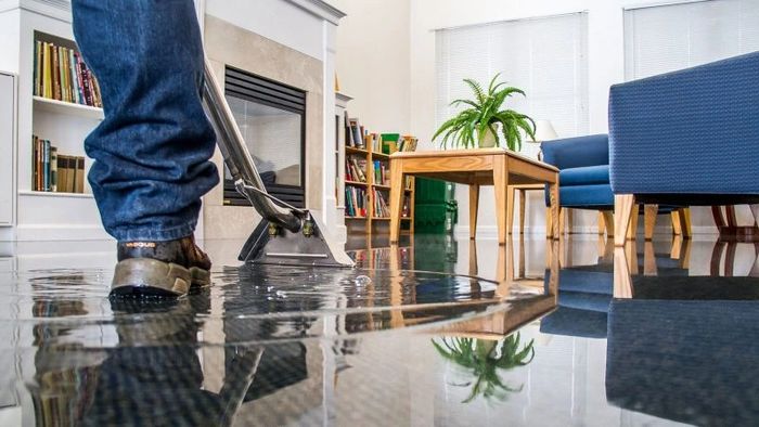 Person cleaning flooded living room floor with a wet vacuum.