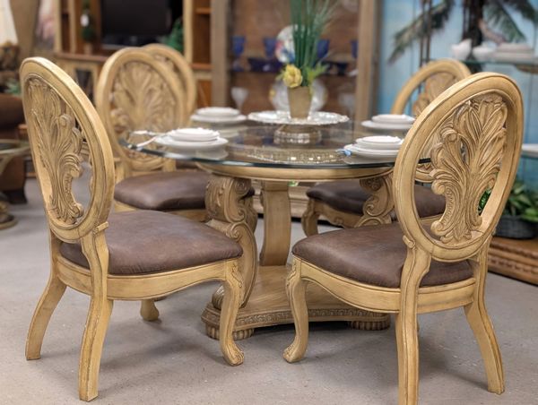 Elegant wooden dining table set with glass top and intricately carved chairs.