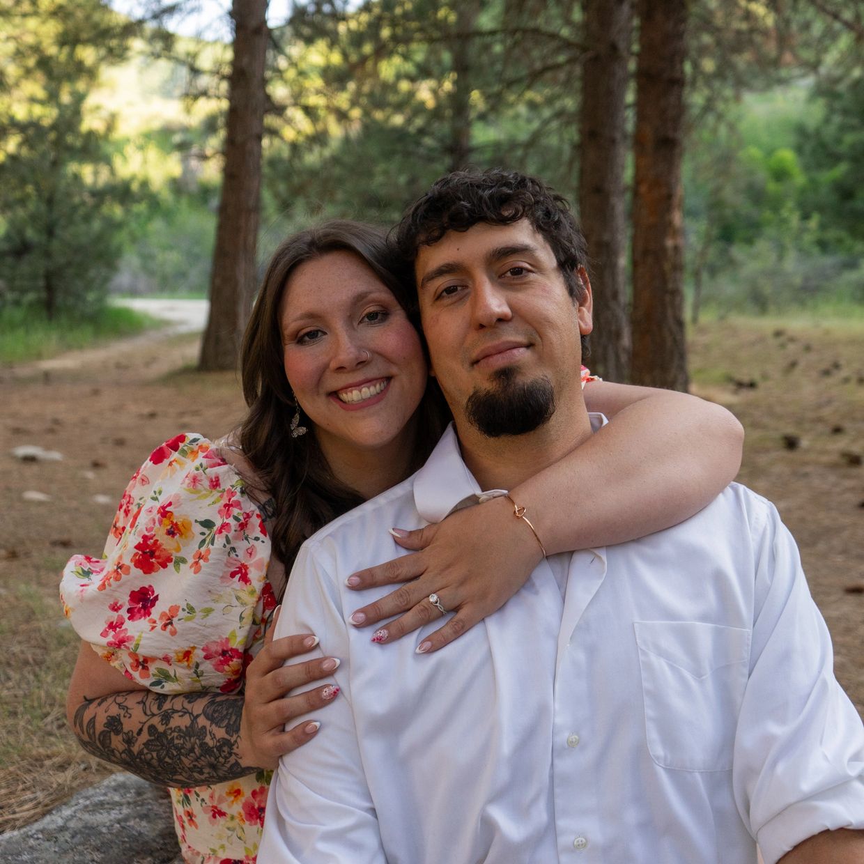 A happy couple embraces outdoors in a forest setting.