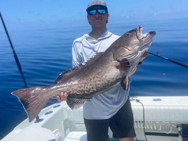 A man on a boat proudly holds a large fish against a calm ocean backdrop.