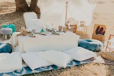 Cozy outdoor picnic setup with cushions and elegant tableware under a white umbrella.