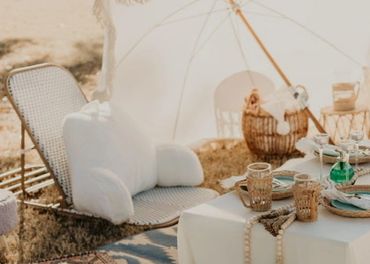 Cozy outdoor picnic setup with cushions, wicker chairs, and a white umbrella.