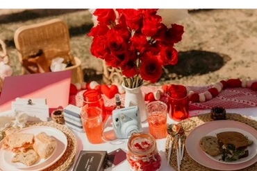 Romantic picnic setup with red roses, sandwiches, and drinks on a sunny day.
