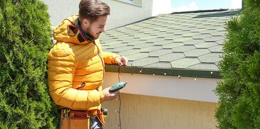 Man installing Christmas lights on a roof edge.