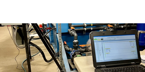 Laptop showing PLC programming software near industrial pipes and valves.