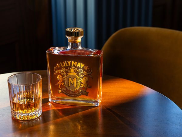 A bottle of Lily May premium bourbon whiskey and a glass on a wooden table.