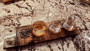 Whiskey tasting flight with one glass partially filled on a wooden board.