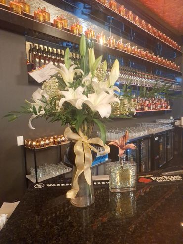 Elegant white lilies in a vase with a golden ribbon on a bar counter.