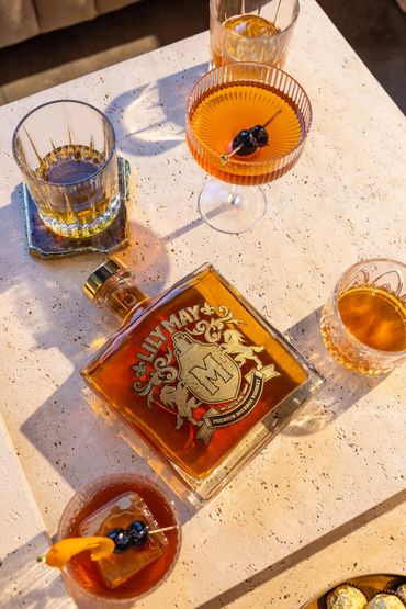 A bottle of Lily May Premium Bourbon Whiskey with various whiskey glasses on a table.