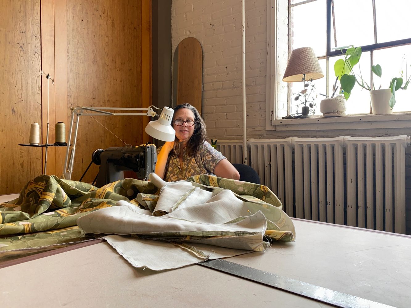 Helen Miller sits at an industrial sewing machine in loft space sewing luxury printed linen