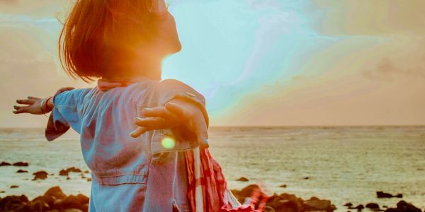 Person enjoying sunset with arms outstretched by the sea.
