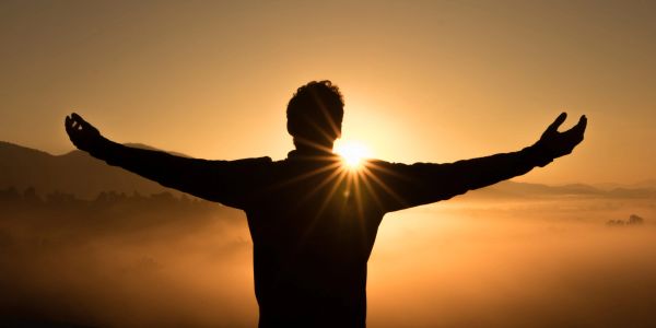 Silhouette of person with arms outstretched at sunrise.