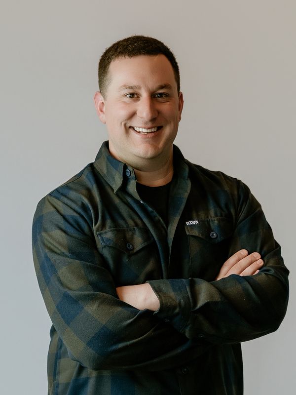 Smiling man in a checkered shirt with arms crossed.