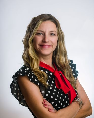 Confident woman with blonde hair wearing a polka dot blouse and red scarf.