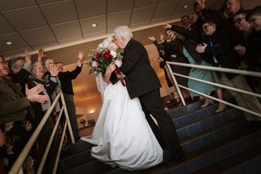 Elderly couple kissing at their wedding surrounded by cheering guests.