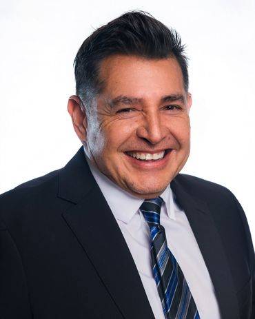 Smiling man in a suit with a blue striped tie against a white background.